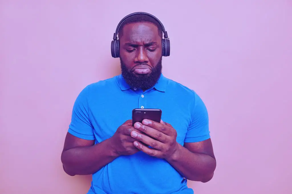 homem negro com fones de ouvido olhando para o celular sem entender a mensagem enviada com ruídos de comunicação