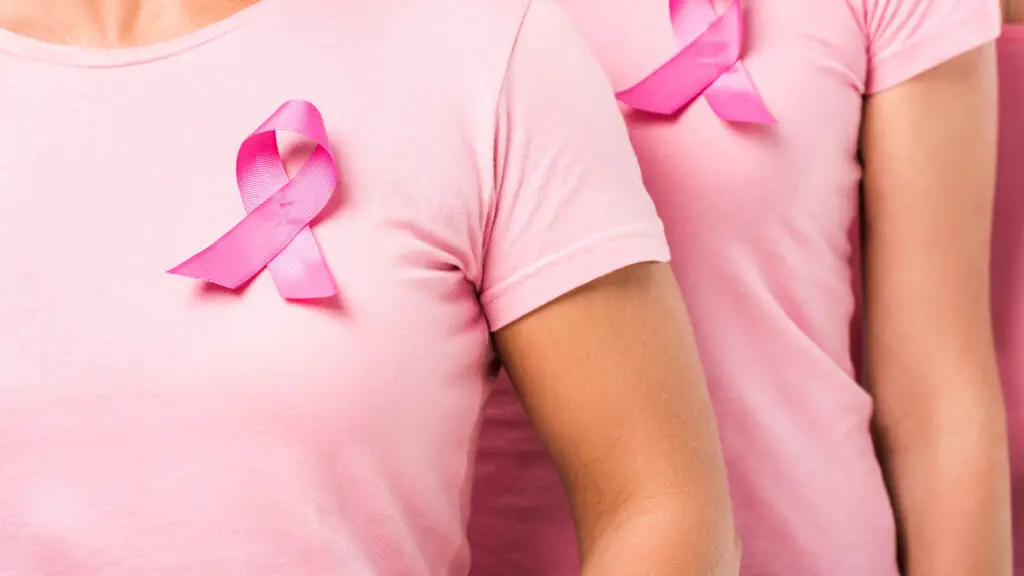 close up do colo de duas mulheres de camiseta cor-de-rosa e o laço característico da campanha Outubro Rosa